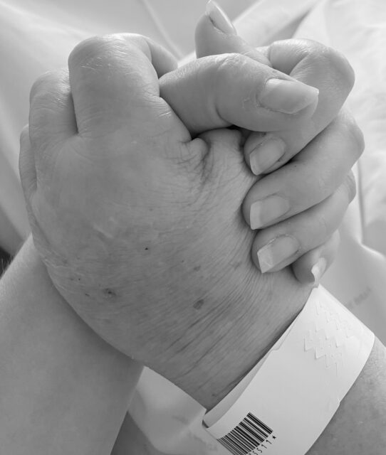 Megan and Diana holding hands while she is in her hospital bed, the hand form a heart clasped together. Black and White image.